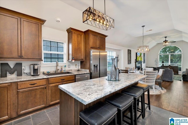 kitchen with appliances with stainless steel finishes, a sink, a kitchen breakfast bar, open floor plan, and lofted ceiling