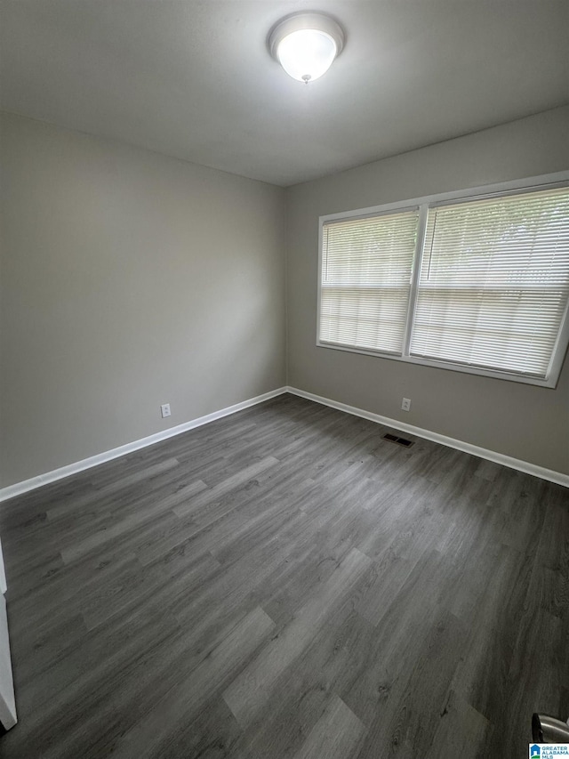 unfurnished room featuring baseboards, dark wood finished floors, and visible vents