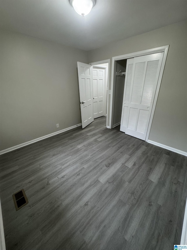 unfurnished bedroom with dark wood-style flooring, baseboards, visible vents, and a closet