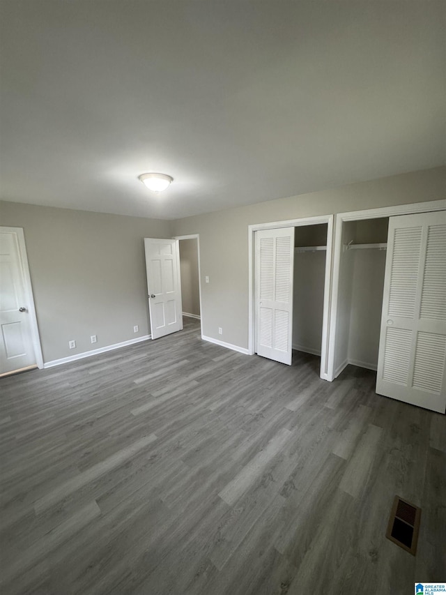 unfurnished bedroom featuring visible vents, dark wood-type flooring, baseboards, and multiple closets