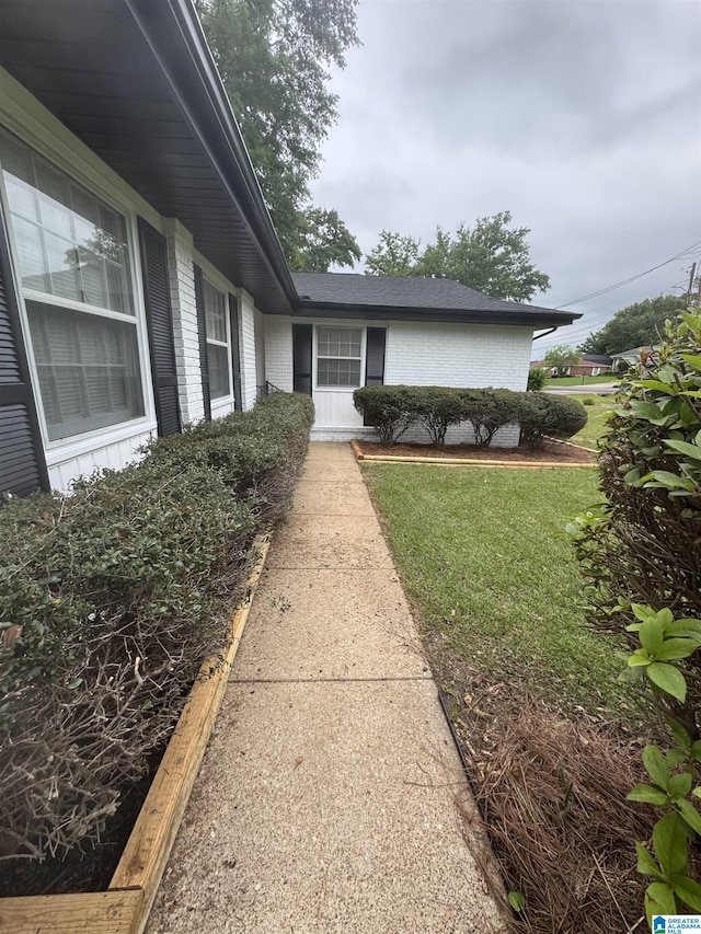view of home's exterior with brick siding, roof with shingles, and a yard