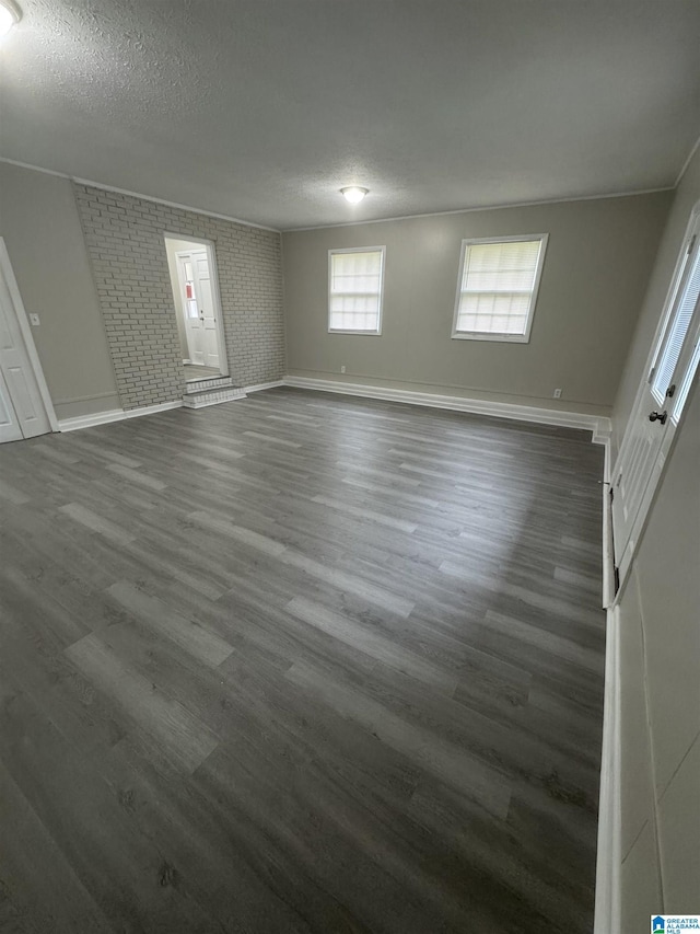 unfurnished bedroom featuring brick wall, baseboards, dark wood-style flooring, and a textured ceiling