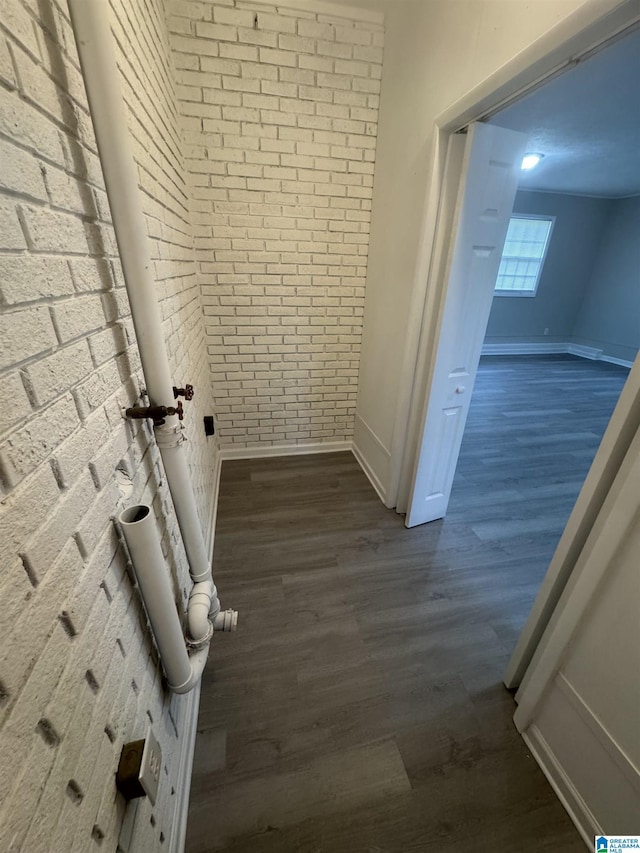 interior space featuring baseboards, dark wood-style flooring, and brick wall