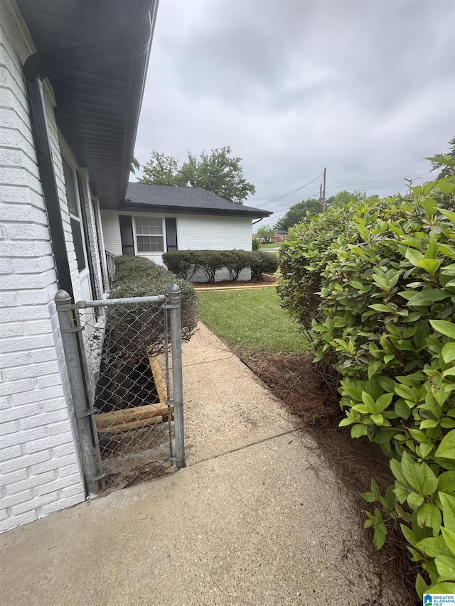 view of property exterior featuring a lawn, a gate, and brick siding