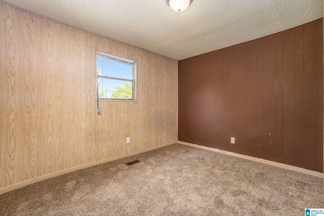 spare room with wooden walls, a textured ceiling, visible vents, and carpet