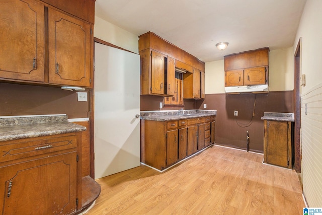 kitchen with brown cabinetry, light wood-style flooring, and under cabinet range hood
