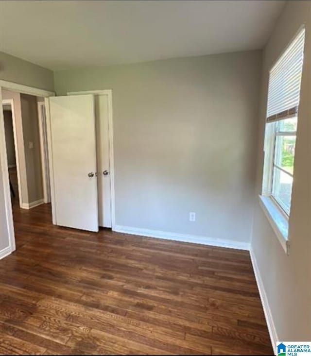 unfurnished bedroom featuring dark wood-style flooring, baseboards, and a closet