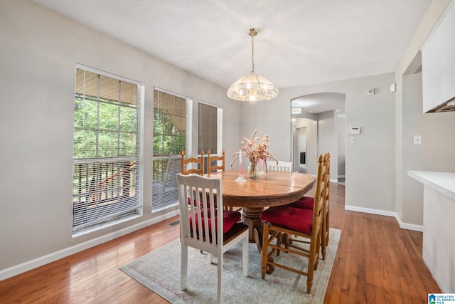 dining area with baseboards, arched walkways, light wood-style floors, and a notable chandelier