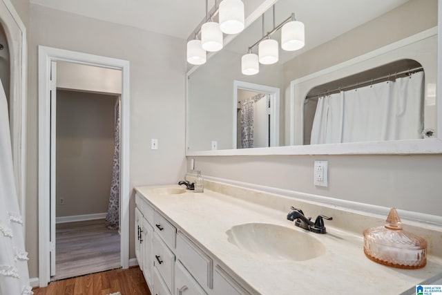 full bath with double vanity, baseboards, a sink, and wood finished floors
