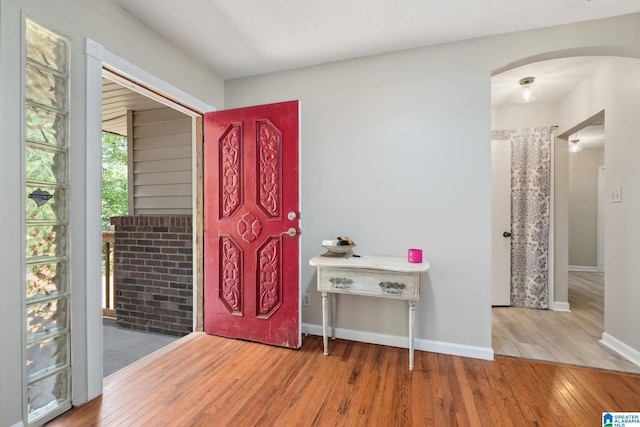 foyer with baseboards, arched walkways, and wood finished floors