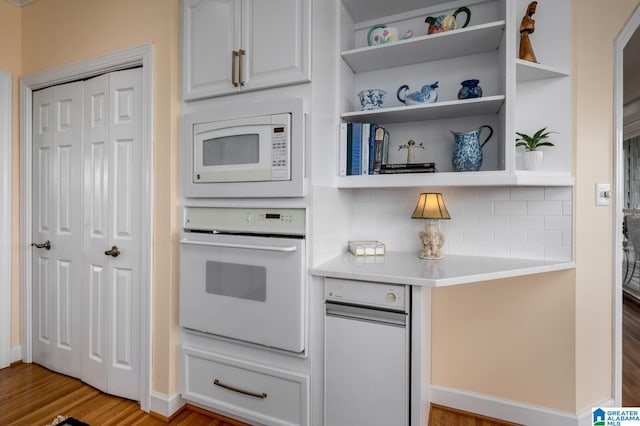 kitchen featuring baseboards, white appliances, light countertops, light wood-style floors, and decorative backsplash