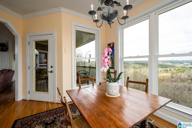 dining space featuring a notable chandelier, baseboards, crown molding, wood finished floors, and arched walkways