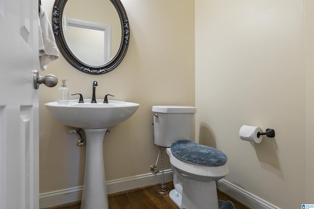 half bathroom with toilet, baseboards, and wood finished floors