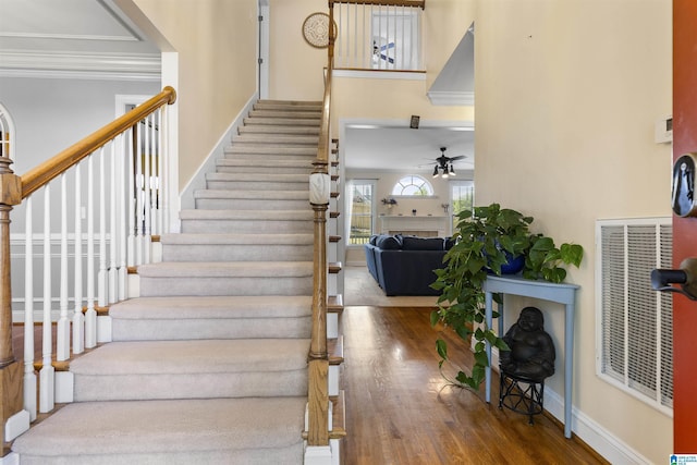 stairway with crown molding, ceiling fan, a high ceiling, wood finished floors, and visible vents