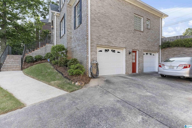 view of side of property with an attached garage, brick siding, driveway, and stairway