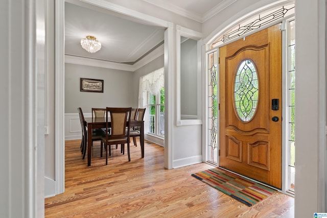 foyer with a healthy amount of sunlight, an inviting chandelier, crown molding, and light wood finished floors