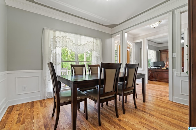 dining space with crown molding, a chandelier, light wood-style flooring, and a wainscoted wall