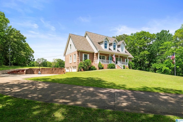 new england style home with a front lawn, an attached garage, brick siding, a porch, and driveway