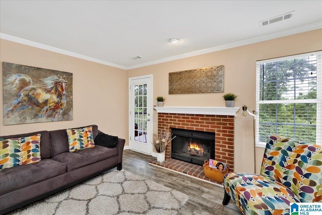 living room with crown molding, a brick fireplace, wood finished floors, and visible vents