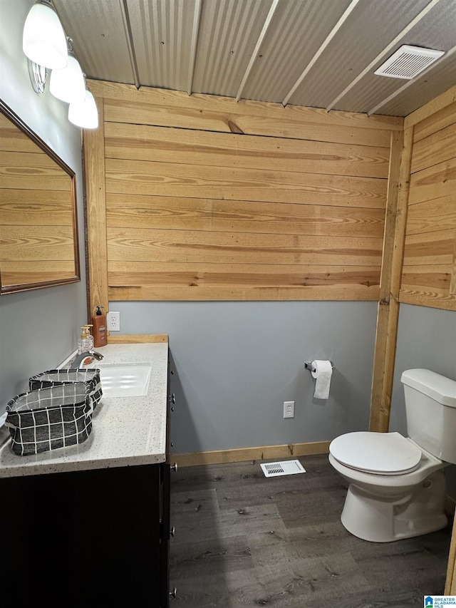 half bathroom with visible vents, wood finished floors, vanity, baseboards, and toilet