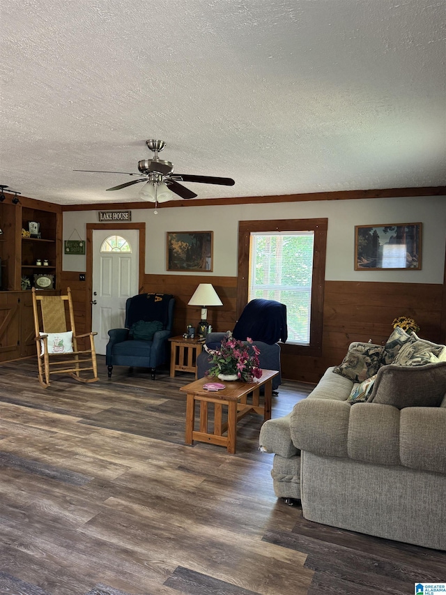 living room with a ceiling fan, a textured ceiling, wainscoting, wood walls, and wood finished floors