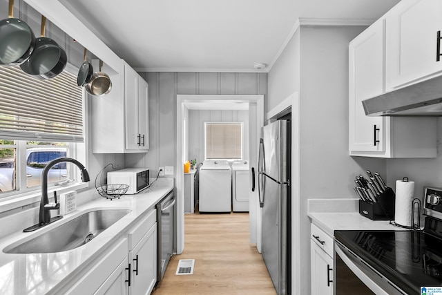kitchen featuring appliances with stainless steel finishes, washing machine and dryer, a sink, crown molding, and under cabinet range hood