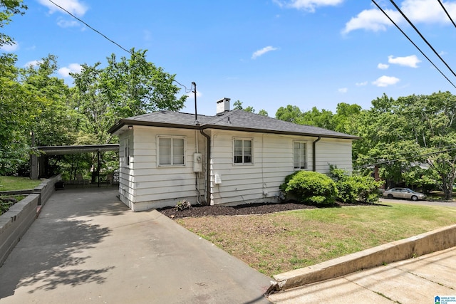 view of front of property featuring concrete driveway, a chimney, a front lawn, and a carport