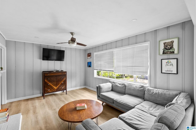 living room with ceiling fan, a decorative wall, light wood-style flooring, ornamental molding, and baseboards