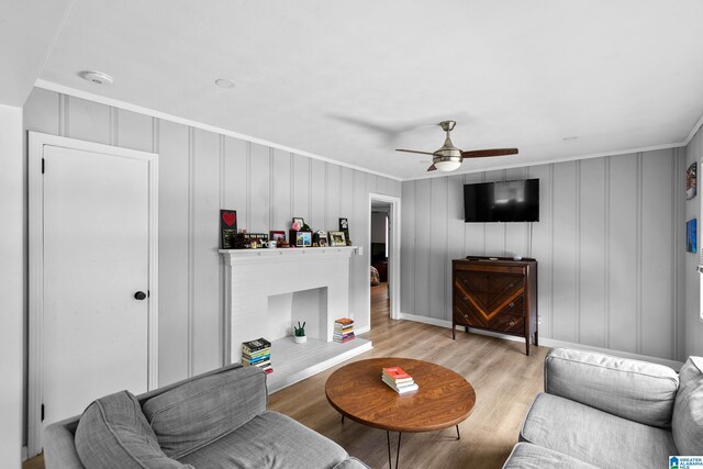 living area featuring ceiling fan, light wood finished floors, crown molding, and a decorative wall
