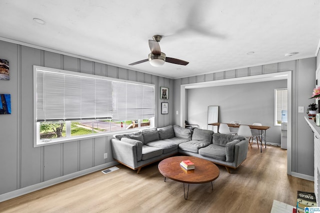 living area with a decorative wall, wood finished floors, a ceiling fan, ornamental molding, and baseboards