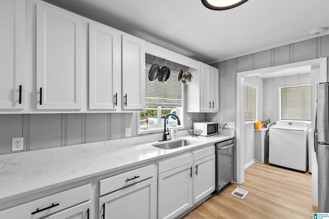 kitchen with washer / dryer, a sink, white microwave, stainless steel dishwasher, and white cabinetry