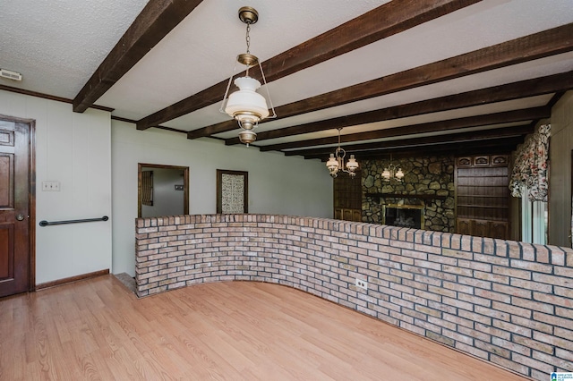 unfurnished room with an inviting chandelier, wood finished floors, beam ceiling, and a large fireplace