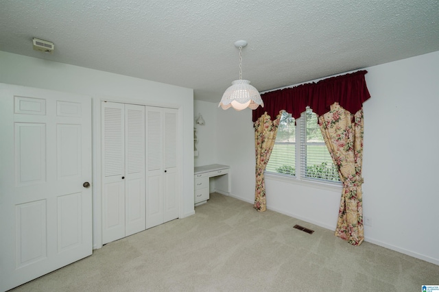 unfurnished bedroom featuring carpet flooring, built in desk, a textured ceiling, visible vents, and a closet