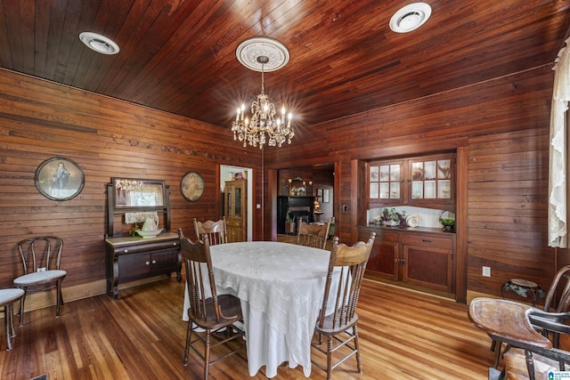 dining space featuring an inviting chandelier, wooden walls, and wood finished floors
