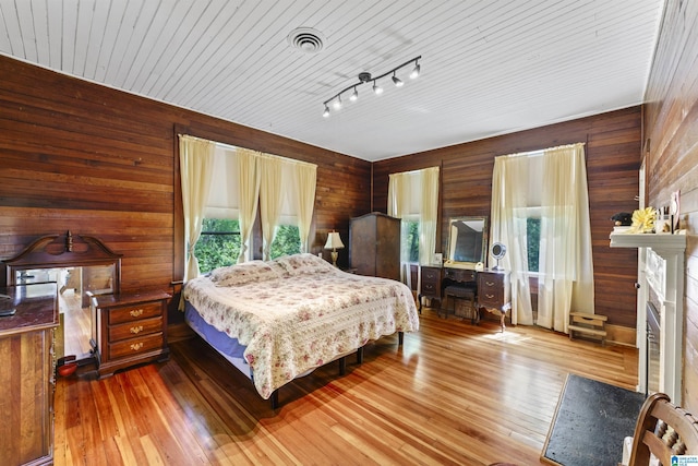bedroom with wooden walls, visible vents, and a fireplace
