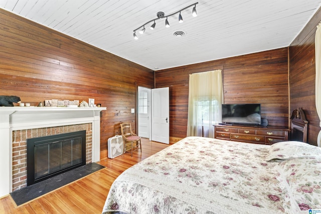 bedroom with wooden walls, a brick fireplace, and wood finished floors