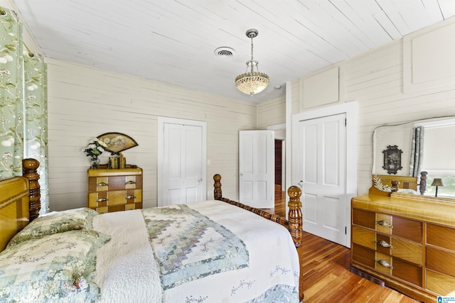 bedroom with wood walls, visible vents, and wood finished floors
