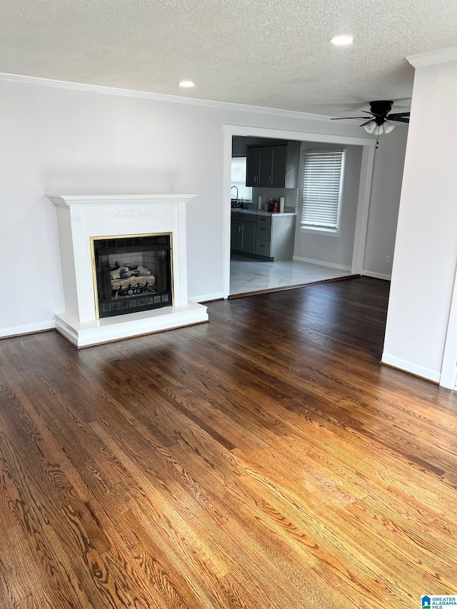 unfurnished living room with dark wood-style flooring, a textured ceiling, ornamental molding, and a fireplace with raised hearth