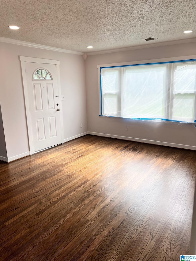 entryway with a textured ceiling, baseboards, wood finished floors, visible vents, and ornamental molding
