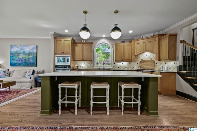 kitchen with ornamental molding, light wood finished floors, appliances with stainless steel finishes, and a center island