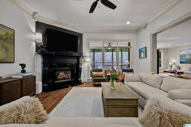 living area featuring a fireplace with flush hearth, wood finished floors, a ceiling fan, and ornamental molding