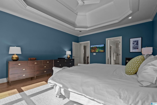 bedroom with ensuite bathroom, wood finished floors, ornamental molding, ceiling fan, and a raised ceiling