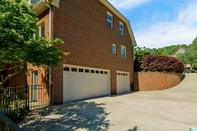 view of side of home with driveway, brick siding, an attached garage, and fence