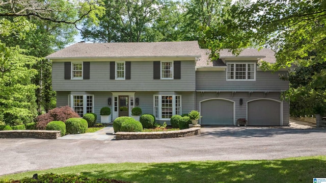 colonial-style house with driveway, a shingled roof, and a garage