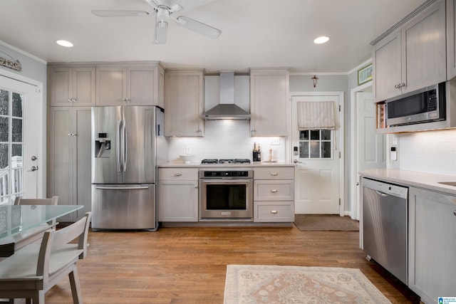 kitchen with wall chimney exhaust hood, crown molding, light countertops, gray cabinetry, and appliances with stainless steel finishes