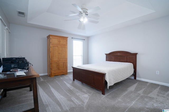 bedroom featuring visible vents, baseboards, light colored carpet, a tray ceiling, and a ceiling fan