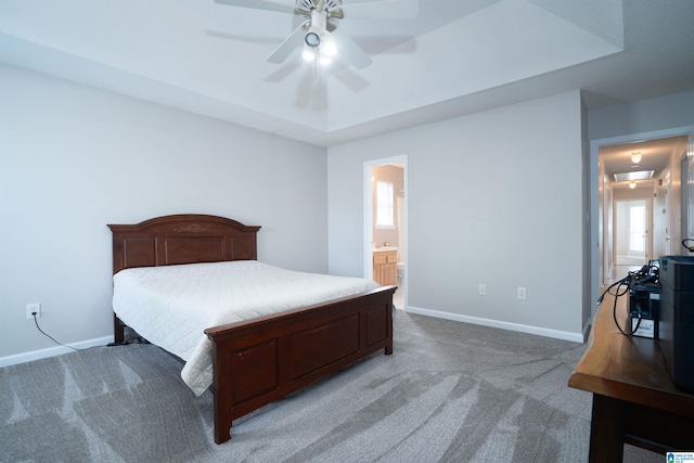 carpeted bedroom with a raised ceiling, baseboards, ensuite bathroom, and ceiling fan