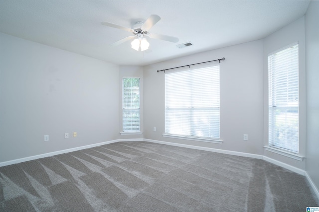 carpeted empty room with baseboards, a ceiling fan, a healthy amount of sunlight, and visible vents