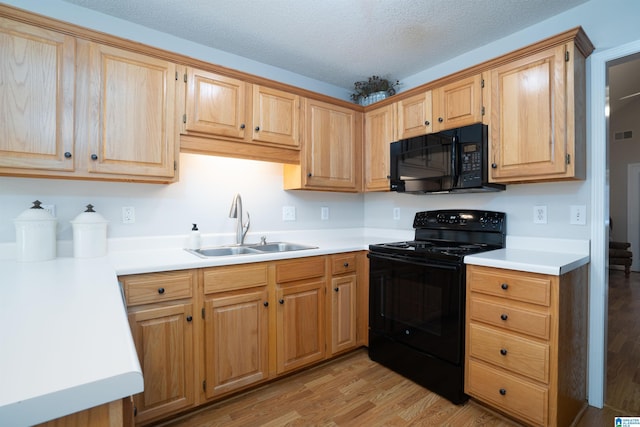 kitchen with light countertops, a sink, black appliances, and light wood-type flooring