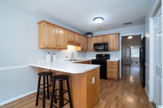 kitchen featuring visible vents, a peninsula, a breakfast bar, a sink, and black appliances
